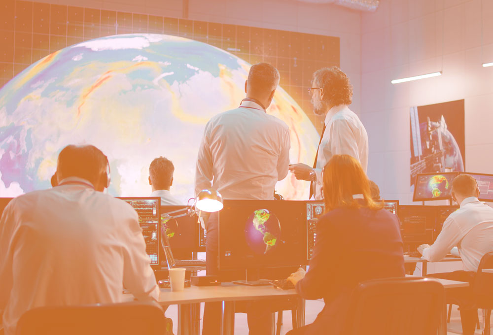 specialized science and engineering concept: image of men and women in a control room with maps of globe on wall and monitors