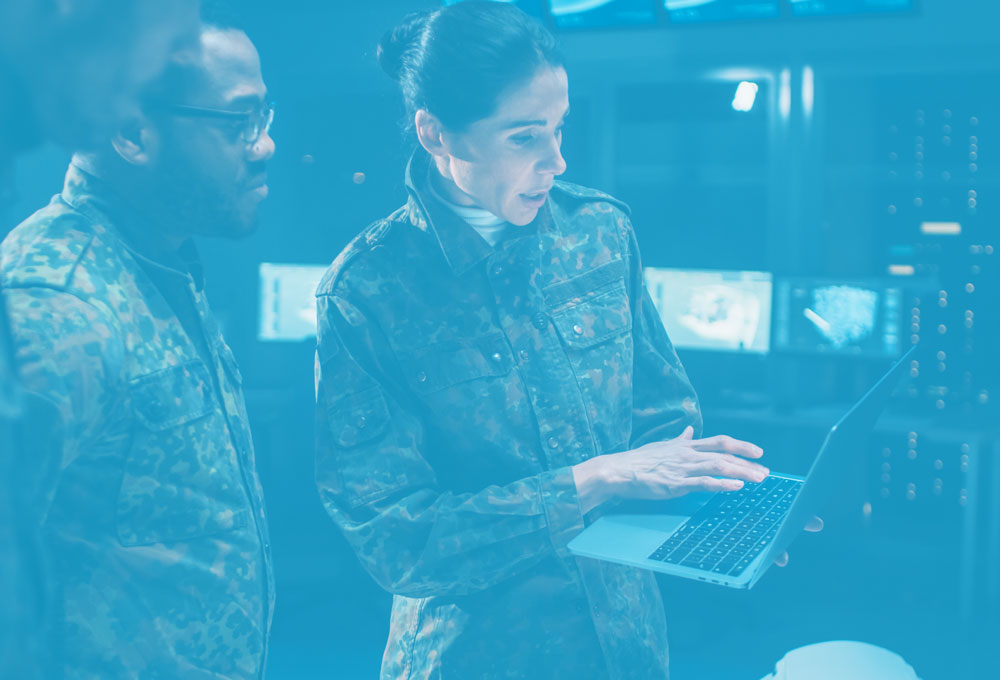 critical mission support concept image: 2 men looking over woman's shoulder as she explains something on her laptop; all 3 in military uniforms